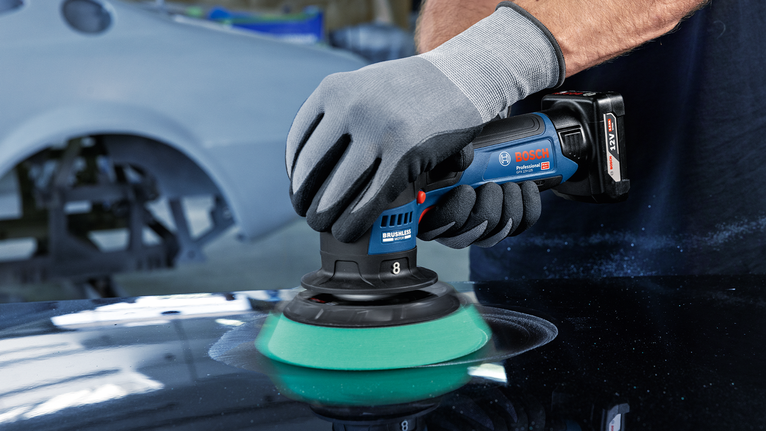 Una persona che indossa un equipaggiamento di sicurezza lucida la superficie di un'auto con un elettroutensile portatile.