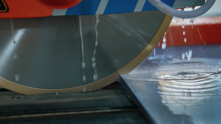 Lama di sega circolare di grandi dimensioni con getto d'acqua che taglia una superficie liscia di piastrelle.