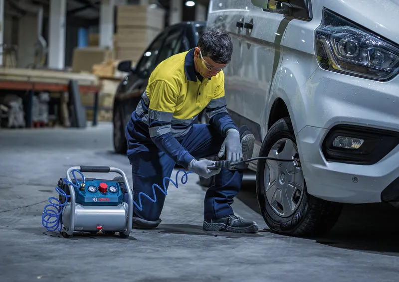 Una persona che indossa l'equipaggiamento di sicurezza gonfia lo pneumatico di un furgone utilizzando un compressore d'aria portatile.
