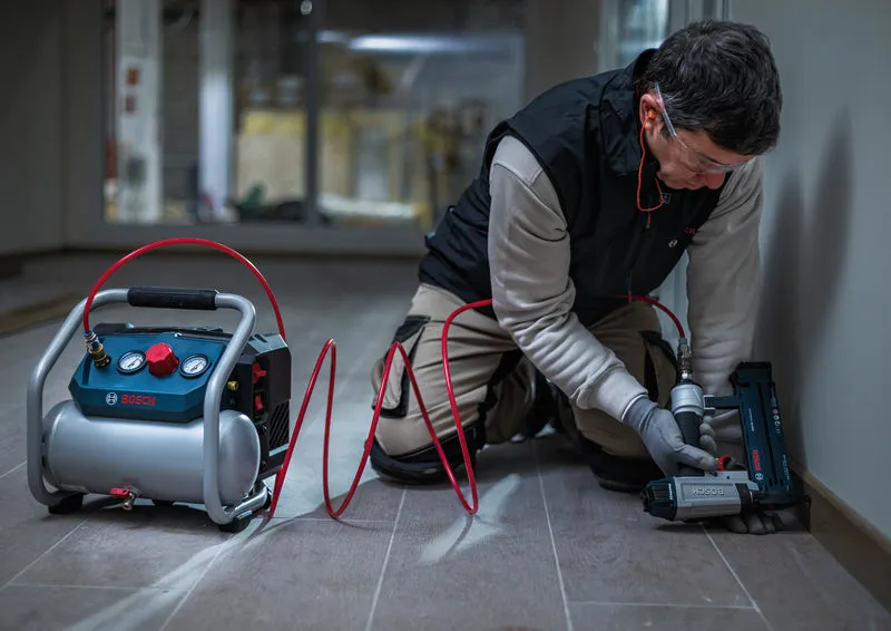 Una persona che indossa un equipaggiamento di sicurezza utilizza un utensile pneumatico per fissare le modanature lungo una parete.