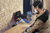 Una persona che indossa dispositivi di protezione individuale utilizza una sega a troncare per tagliare una tavola di legno.