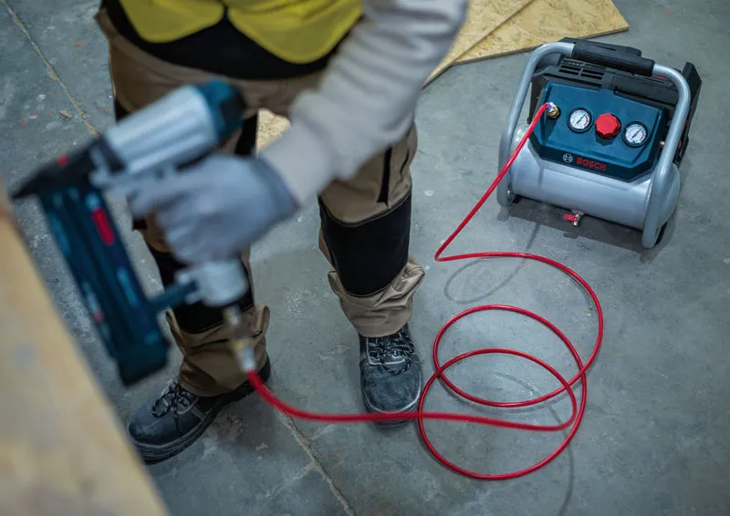 Una persona che indossa un equipaggiamento di sicurezza utilizza una pistola sparachiodi pneumatica collegata a un compressore d'aria.