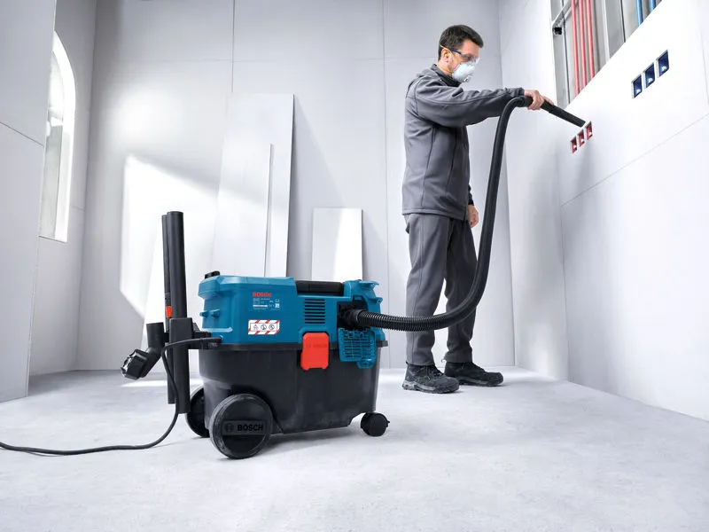 Una persona che indossa dispositivi di protezione individuale utilizza un aspiratore multiuso per pulire le prese elettriche a muro.