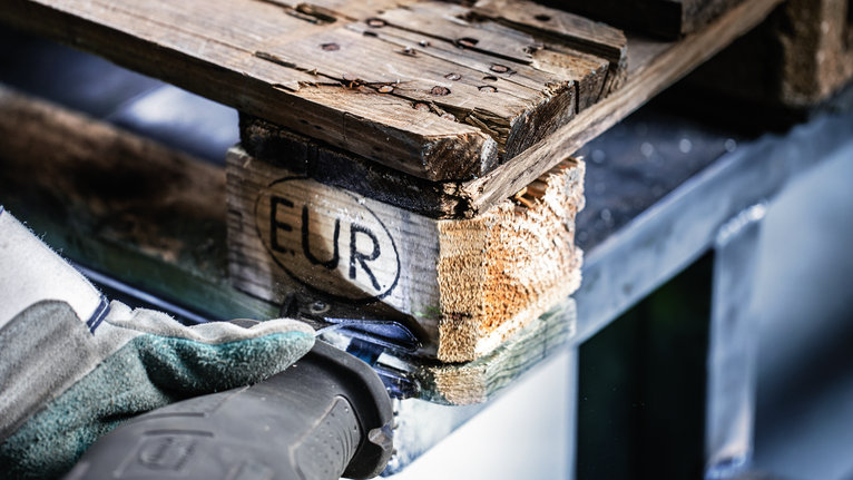 Una persona che indossa dispositivi di sicurezza taglia un pallet di legno con un seghetto alternativo.