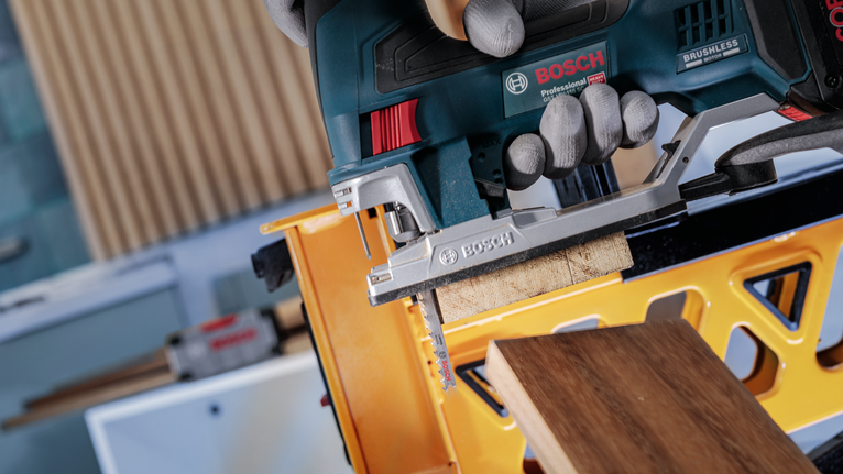 Una persona che indossa un equipaggiamento di sicurezza taglia una tavola di legno con un seghetto alternativo.