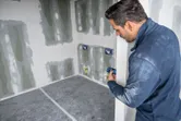 Persona che utilizza un misuratore laser per rilevare le dimensioni in una stanza parzialmente terminata.