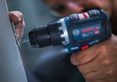 Una persona utilizza un trapano avvitatore a impulsi senza fili per stringere le viti di una cerniera metallica.