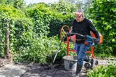 Una persona che indossa dispositivi di protezione individuale utilizza un utensile elettrico per impastare il calcestruzzo all'aperto.