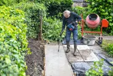 Una persona che indossa dispositivi di protezione individuale utilizza un utensile elettrico per compattare il calcestruzzo su un vialetto da giardino.