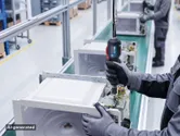 Una persona che indossa dispositivi di protezione individuale utilizza un utensile elettrico per assemblare un forno a microonde su una linea di produzione.