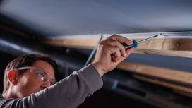 Una persona che indossa dispositivi di protezione individuale fissa una vite a un telaio del soffitto con un utensile manuale.