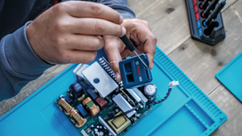 Una persona ripara un circuito stampato elettronico utilizzando un cacciavite.