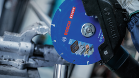 Una persona con indosso dispositivi di protezione individuale taglia del metallo utilizzando una grande lama di sega circolare.