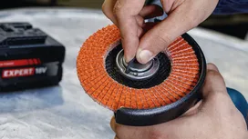 Una persona sostituisce un disco su una smerigliatrice angolare, accanto a un pacco batterie ben visibile.
