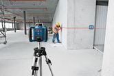 Una livella laser montata su un treppiede proietta una linea mentre una persona, munita di dispositivi di sicurezza, traccia una linea su una parete.