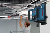 Uno strumento di livellamento laser montato a parete proietta una linea rossa mentre una persona lavora sul soffitto.