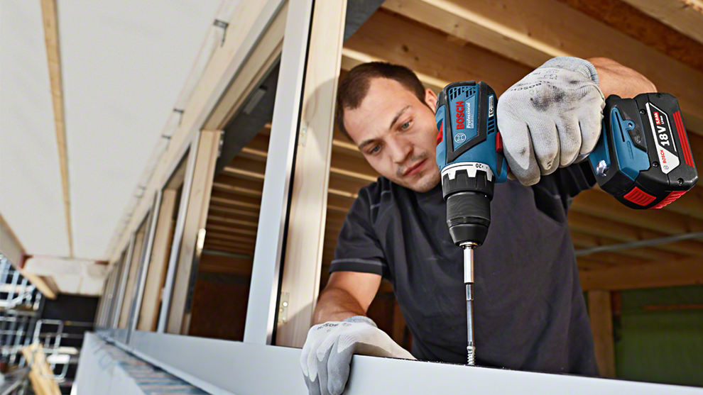 Un artisan avec une perceuse sans fil Bosch Professional monte une structure métallique.