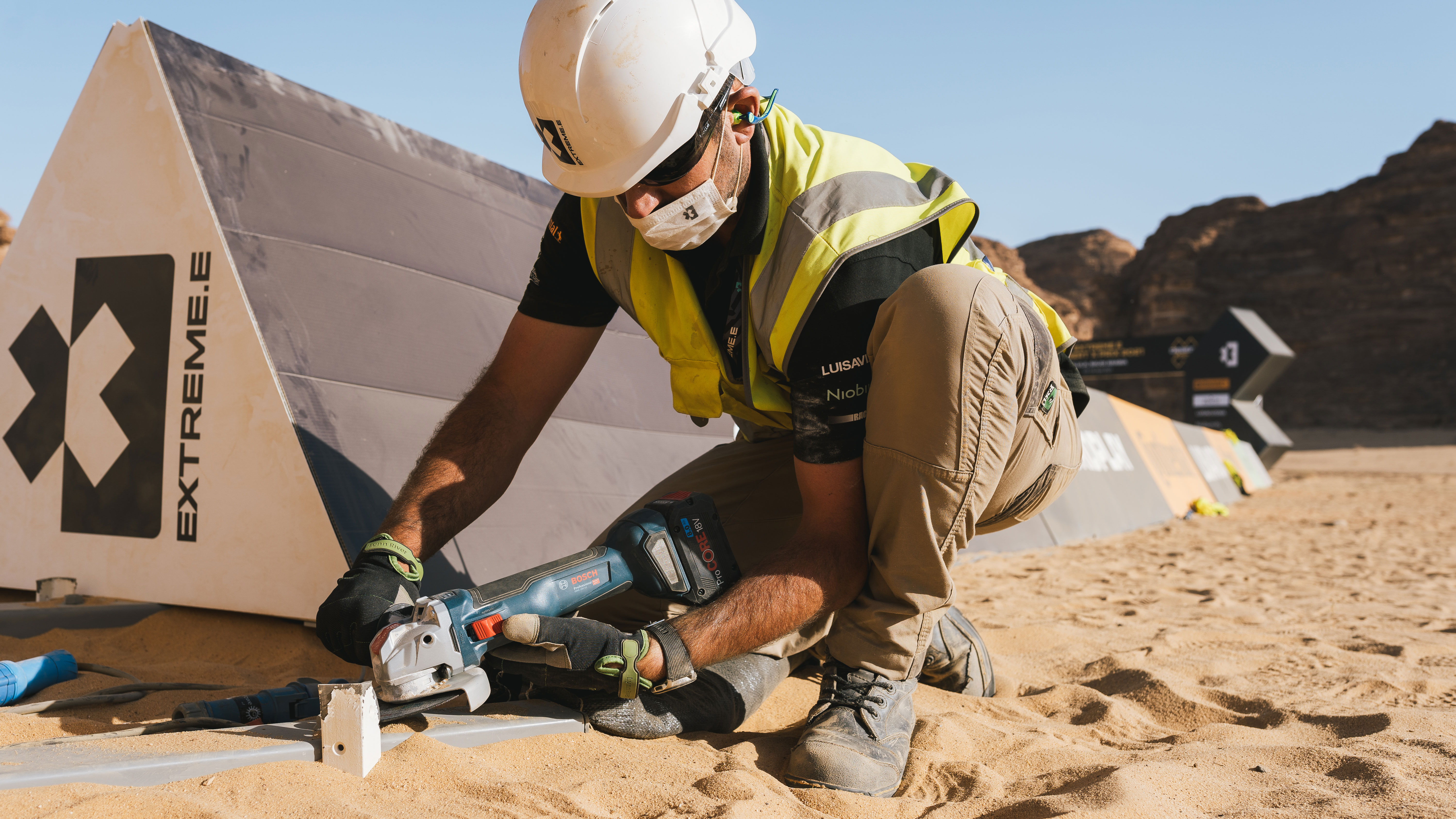 Ein Arbeiter in Warnweste schneidet mit einer Bosch Maschine in den Sand.