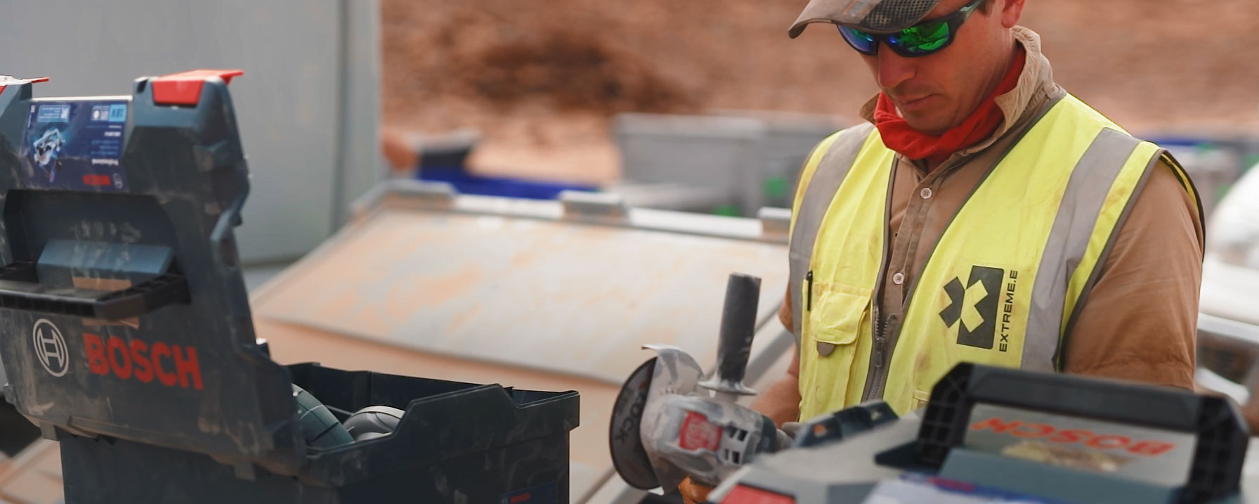 Ein Arbeiter mit gelber Weste hält eine Bosch-Werkzeugkiste auf einer Baustelle.