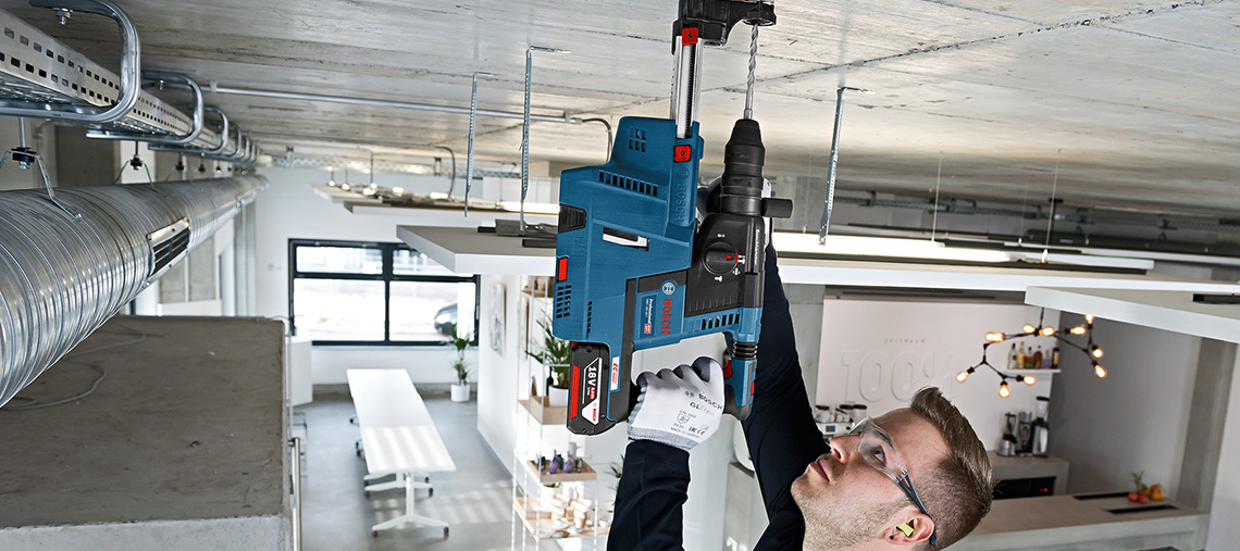 Ein handwerklich tätiger Mann nutzt einen blauen Bosch Professional Bohrer über Kopf.