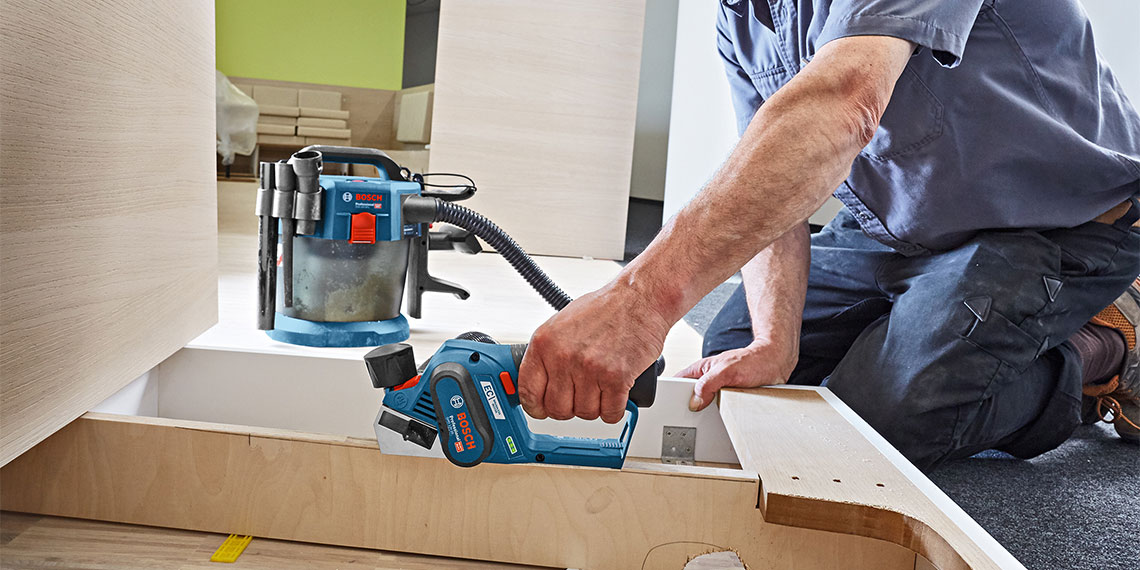 Ein Handwerker benutzt einen blauen Bosch Professional Elektrohobel auf Holz.