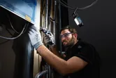 Una persona que usa equipo de seguridad perfora una pared y una luz inalámbrica ilumina el espacio de trabajo.