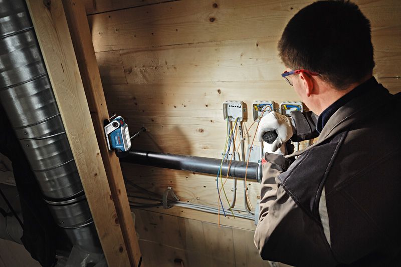 Una persona que usa equipo de seguridad trabaja con cableado eléctrico bajo una luz inalámbrica brillante.