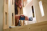 Una persona que usa equipo de seguridad corta una tabla de madera con una herramienta multiusos inalámbrica.