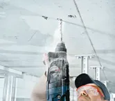 Una persona que usa equipo de seguridad perfora un techo de hormigón.