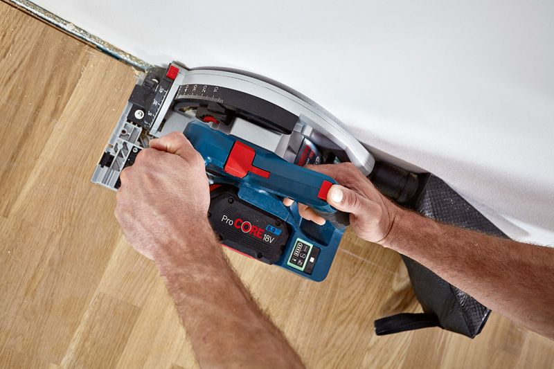 Una persona opera una sierra circular inalámbrica para cortar pisos de madera cerca de una pared.