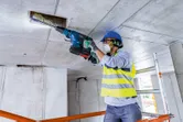 Una persona que usa equipo de seguridad perfora un techo de hormigón con un martillo perforador.