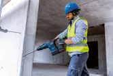 Una persona que usa equipo de seguridad perfora una pared de hormigón con un martillo perforador inalámbrico.