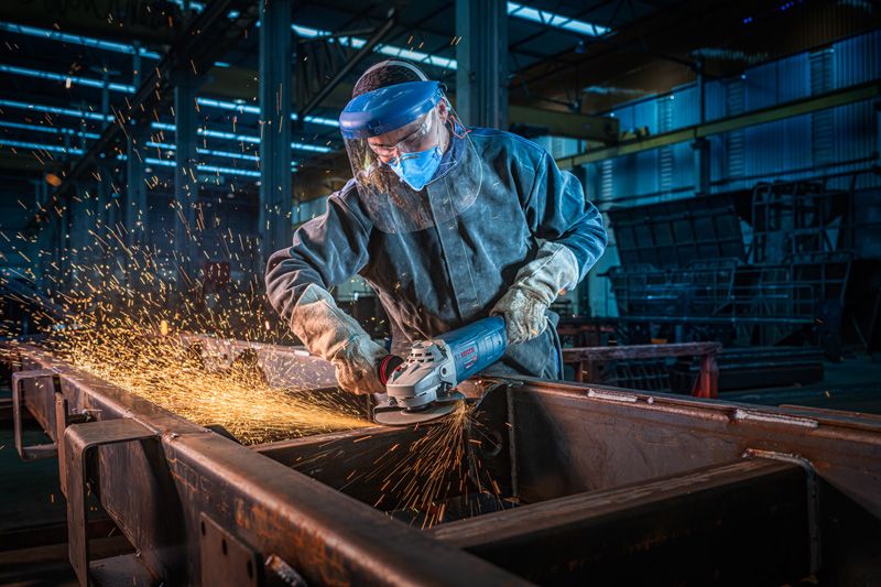 Una persona que usa equipo de seguridad muele vigas de metal con una amoladora angular, saltando chispas.