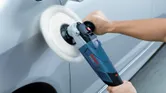 Una persona utiliza una pulidora para pulir la superficie de un coche.