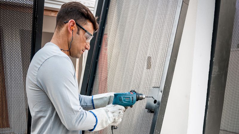 Una persona que usa equipo de seguridad perfora un marco de metal utilizando un taladro de impacto.