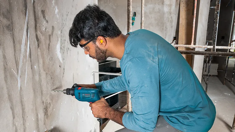 Una persona que usa equipo de seguridad perfora una pared de hormigón utilizando un taladro de impacto.