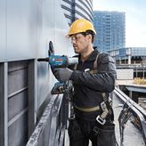 Una persona que usa equipo de seguridad utiliza un taladro eléctrico para fijar paneles en el exterior de un edificio.