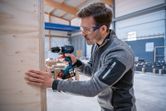 Una persona que usa equipo de seguridad perfora una tabla de madera dentro de un taller.