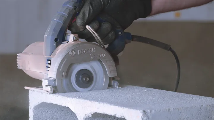 Una persona que usa equipo de seguridad utiliza una sierra circular para cortar un bloque de hormigón.