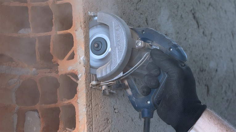 Una persona que usa equipo de seguridad corta una ranura en una pared de hormigón utilizando una sierra circular eléctrica.