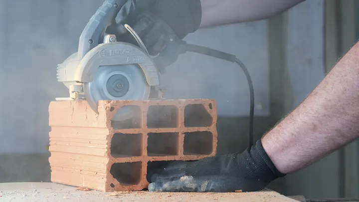 Una persona que usa equipo de seguridad corta un bloque de ladrillo con una sierra circular.