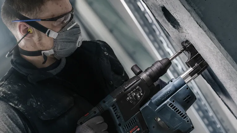 Una persona que usa equipo de seguridad perfora hormigón con un martillo perforador.