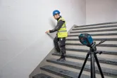 Una persona que lleva puesto un equipo de seguridad utiliza un nivel láser para marcar una línea en la pared de una escalera.