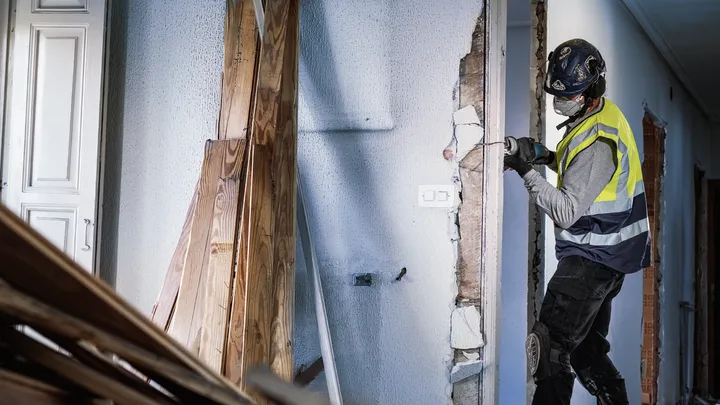 Una persona que usa equipo de seguridad perfora una pared durante una renovación.
