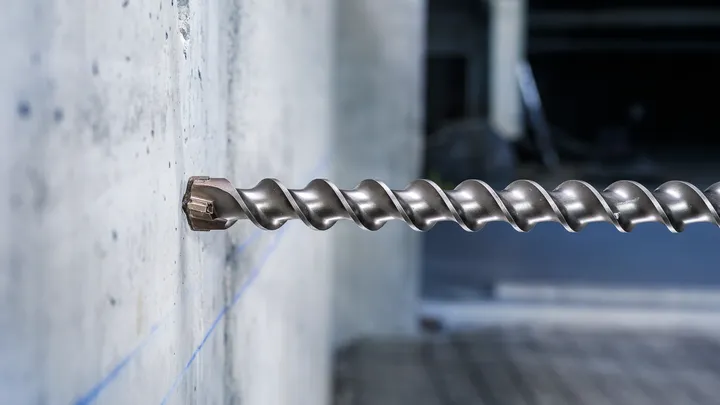 Broca de mampostería de gran tamaño insertada en una pared de hormigón en un entorno industrial.