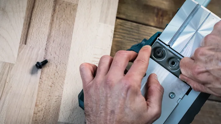 Persona ajustando una pieza metálica de una herramienta eléctrica sobre una superficie de madera.