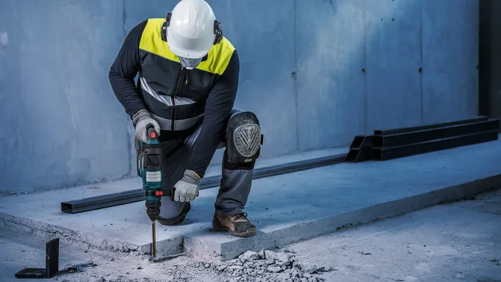 Una persona que usa equipo de seguridad utiliza un taladro eléctrico para romper hormigón.