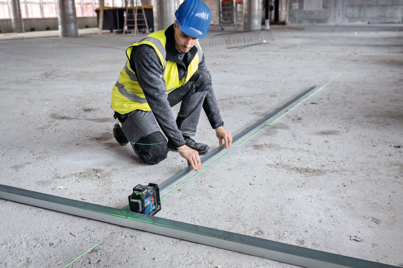 Una persona, equipada con material de seguridad, alinea los rieles metálicos utilizando un nivel láser en una planta de construcción.