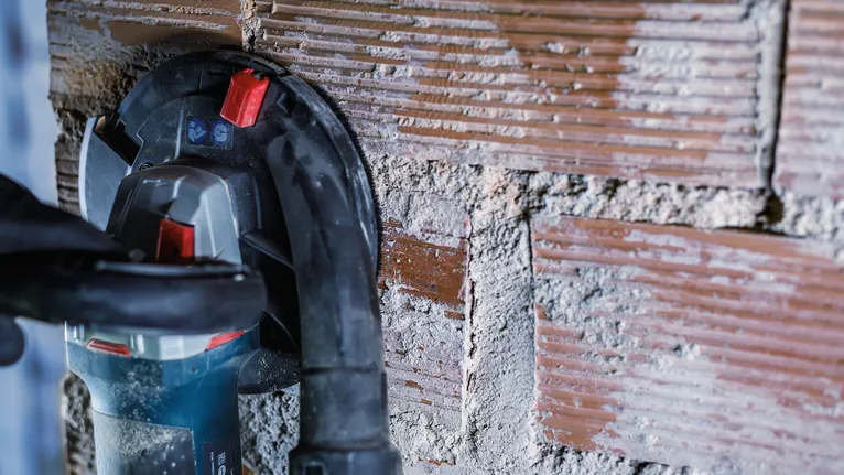 Una persona que usa equipo de seguridad hace una ranura en una pared de ladrillos.