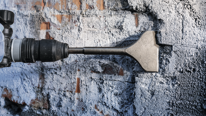 Martillo cincel rompiendo un muro de hormigón durante un proceso de demolición.